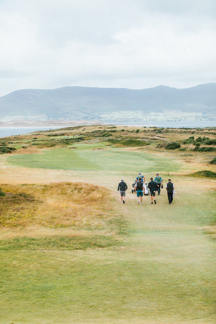 Group of golfers walking on a golf course with mountains in the background