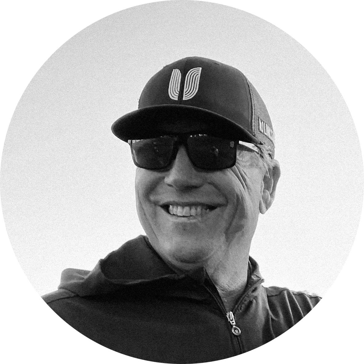 Black and white circular profile picture of Hank Ashworth wearing a cap and sunglasses with a logo.