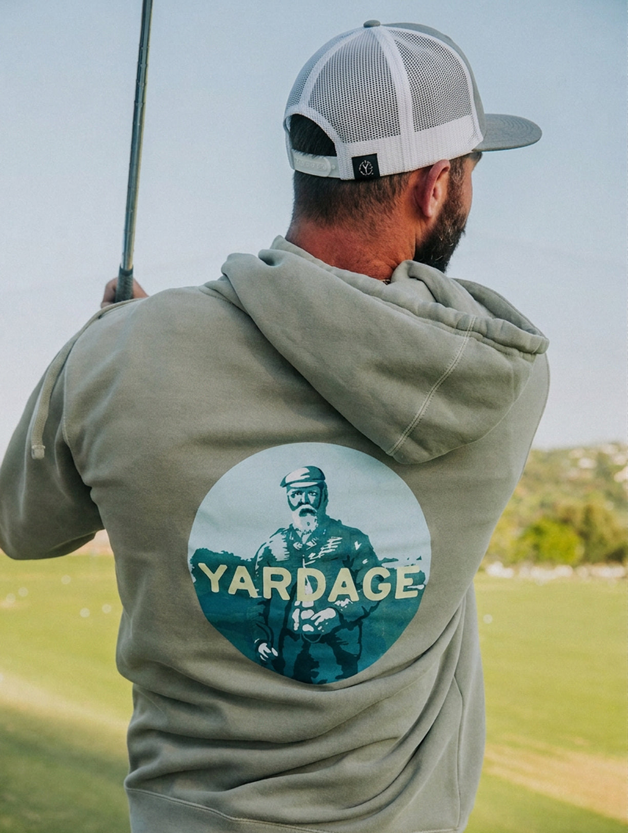 Man wearing a hoodie with 'Yardage' logo on a golf course