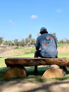 man sitting on a beanch ata golf course wearing the blue Yardage Golf Co ribbon tee
